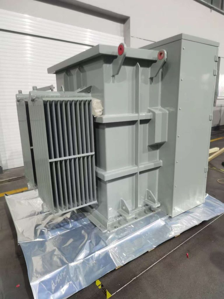Angled view of a grey oil-immersed substation transformer with corrugated cooling fins and enclosed LV cabinet, on shipping pallet